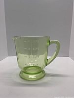 Front view of green uranium glass measuring cup showing measurement markings and handle.
