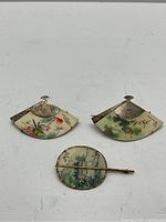 Front view of three brooches styled as traditional Chinese fans with hand-painted scenes and metal details.