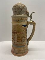 Front side of the stein showing detailed molded relief of buildings and trees by the river.
