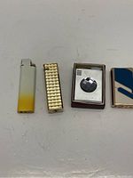 Four vintage lighters displayed in a row on a white surface, showing general appearance and condition.