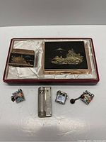 Full set of seven vintage lighters displayed with the Japanese-style lacquered case inside a red frame and white silk-lined interior.