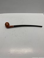 Full view of long wooden pipe with black stem.