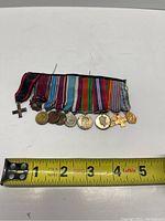 Collection of war medals on ribbon bar with measuring tape showing size about 5 inches wide.