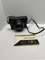 Black leather carrying case with Yashica label on cover and user manual booklet on white surface