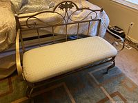 Front view of metal framed bench with cushioned seat, showing decorative backrest and overall shape.