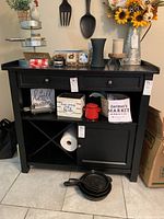 Full view of black wooden kitchen cabinet with a drawer, open shelving that includes a wine rack space, a closed cabinet door, and various decorative items on top and inside shelves.