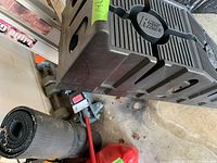 Photo showing stacked Rhino branded plastic car ramps along with a coiled black mat and a red fuel container on garage floor.