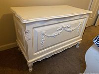 Front and side view of white painted wood chest with carved floral garland applique on front panel and cabriole legs.