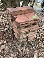 Stack of red clay lawn border pieces with interlocking underside design sitting on leaf-covered ground.