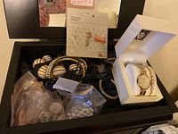 Wide shot of box containing assorted costume jewelry including bracelets, pins, bags with beads, and Anne Klein watch in box.