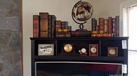Long view showing decorative boxes arranged like books on a shelf, five mantle clocks below, and a globe sculpture on the center top.