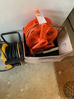 Photo showing two extension cord reels (one orange and one black/yellow) and a box holding loose cords.