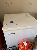 Angle view of the top and front of the white HEC chest freezer showing surface wear and a label with lot number.