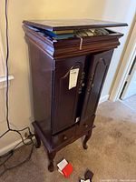 Closed front view of the dark wood jewelry armoire standing on curved legs with two bottom drawers and two front doors. The flip top lid is slightly open.