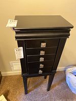 Front view of the black wooden jewelry cabinet with five drawers and legs, showing its general condition and size