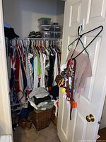 Wide view of closet with hanging clothing, shoes on floor, purses on door