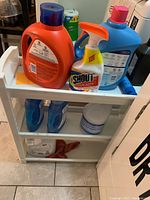 Front view of white laundry caddy filled with various cleaning products including laundry detergent, fabric softener, dish soap, stain remover, and bleach.