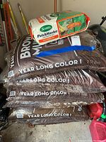 Overall lot showing five bags of brown mulch stacked and one bag of the Scotts PatchMaster lawn repair mix on top.