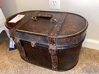 Two angled photos showing a vintage leather-textured lidded box with buckle straps, a handle, and floral embossing on the exterior surface, housing the office supplies.