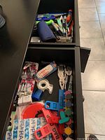 Photo showing open drawers with assorted pens, markers, multitool, clips, tape, battery packs, and other stationary and household items
