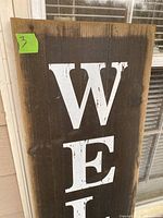 Photo of top half of wooden welcome sign with white W and E letters on dark wood.
