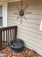 Round metal fire pit resting near deck railing on ground covered with leaves, showing rust and weathered condition.