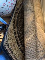 Rolled areas of the round patterned rug showing details of intricate floral and geometric design in cream, navy blue, and beige tones.