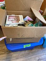 Cardboard box filled with printed sewing pattern envelopes atop a blue plastic tote