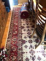 Full length view of the rug showing the detailed floral pattern in red, beige and dark accents, and a rolled section at one end.