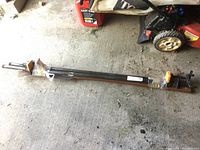 Full view of the pair of long bar clamps lying on concrete floor, showing black metal bars and orange clamp faces taped with plastic wrap.