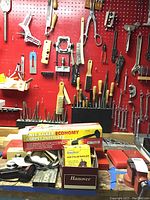 Image of various hand tools including chisels, files, Air Palm Nailer, Knee Kicker Economy Carpet Installer, wrenches, brushes, pipe cutter, and manual hand planer, arranged on a red pegboard and bench area.