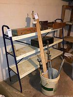 Shelving unit showing a metal vintage Craftsman toolbox, pipe clamps in a bucket, wood pieces, Handy Andy child's carpenter set, and other tools.