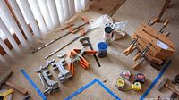 Various clamps, plate joining biscuits in sealed bags, multiple tape measures, and woodworking cans on floor with blue tape outline.
