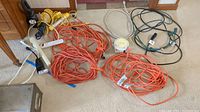 Overview of all items including extension cords, surge protectors, outlet timer, and work lights on carpet floor.