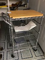 Front view of metal kitchen cart with wooden cutting board top and three wire baskets on wheels.