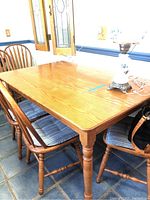 Oak dining table with 4 matching chairs with blue cushions in a tiled room. Table has rounded corners and turned legs.