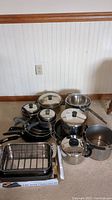 Photo showing set of various kitchen pots and pans with lids and roasting pan on countertop.