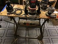 Black & Decker Workmate table with multiple power tools on top, including routers and sander.
