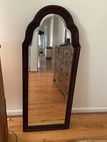 Full view of the tall, arch top Thomasville wall mirror with dark wood frame and beveled glass reflecting a hallway and dresser.