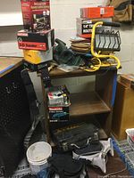 Photo showing stacked boxes including Craftsman 3-D Sander, Makita 4-inch disc grinder, Chicago 1/4 trimmer router, Black & Decker work light, sanding discs and other items on a table and floor.