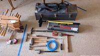 Full overview of lot showing various hammers, crowbars, clamps, tape measures, wire fish tape, toolboxes and tool bag arranged neatly on carpeted floor.