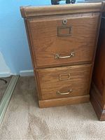 Front view of the small two-drawer wooden filing cabinet with brass hardware and lock.