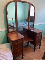 Photo of 6 drawer wooden vanity with tri-fold mirror showing dark wood finish and drawer detail.