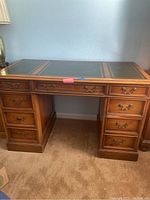 Front view of wooden desk showing nine drawers and leather inlaid top panels.