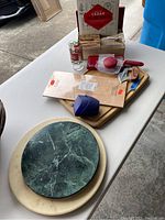 Photo showing various kitchen supply items arranged on tables, including wooden cutting boards, glass, kitchen utensils, and packaged items.