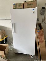 White upright freezer standing next to cardboard boxes in a garage