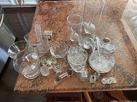 Overview of assorted clear glass items including oil lamps, vases, patterned dishes, and salt and pepper shakers displayed on a countertop.