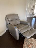 Gray leather rocker recliner chair shown partially reclined with footrest extended in a room with dark wood flooring.