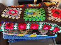 Stack of four crocheted afghans showing colorful granny square and floral designs with different yarn colors and patterns.