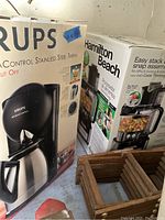 Boxes of kitchen appliances including Krups coffee maker and Hamilton Beach food processor, showing product details on packaging.